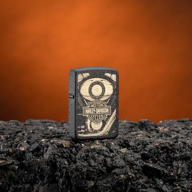 Lifestyle image of Harley-Davidson® 1941 Replica Black Crackle Windproof Lighter standing on asphalt with an orange background