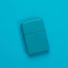 Lifestyle image of Classic Flat Turquoise Windproof Lighter laying on a turquoise surface