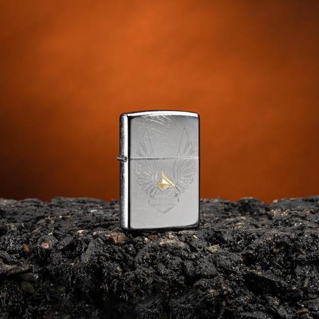 Lifestyle image of Harley-Davidson® Eagles Logo Chrome Arch Windproof Lighter standing on asphalt with an orange background
