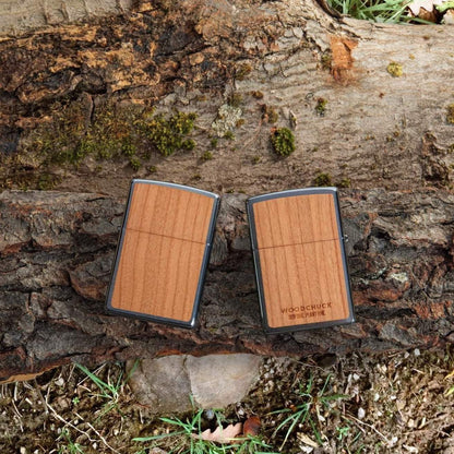 Lifestyle image of WOODCHUCK USA Cherry Emblem Windproof Lighter, laying on a log with one lighter showing the front and the other showing the back