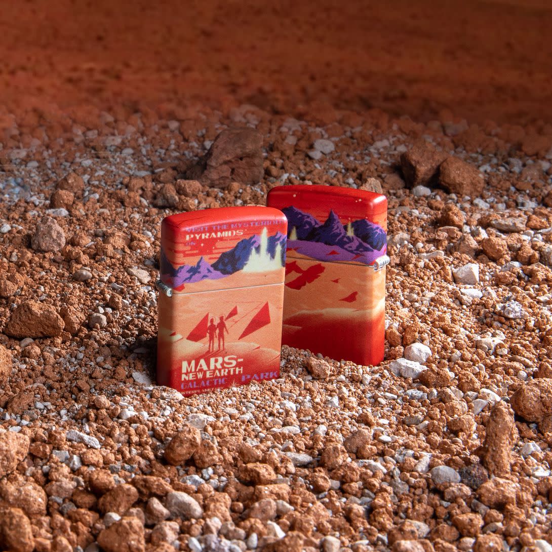 Lifestyle image of two Mars 540 Color Design Windproof Lighters standing on the Mars surface, one lighter showing the front of the design and the other showing the back.